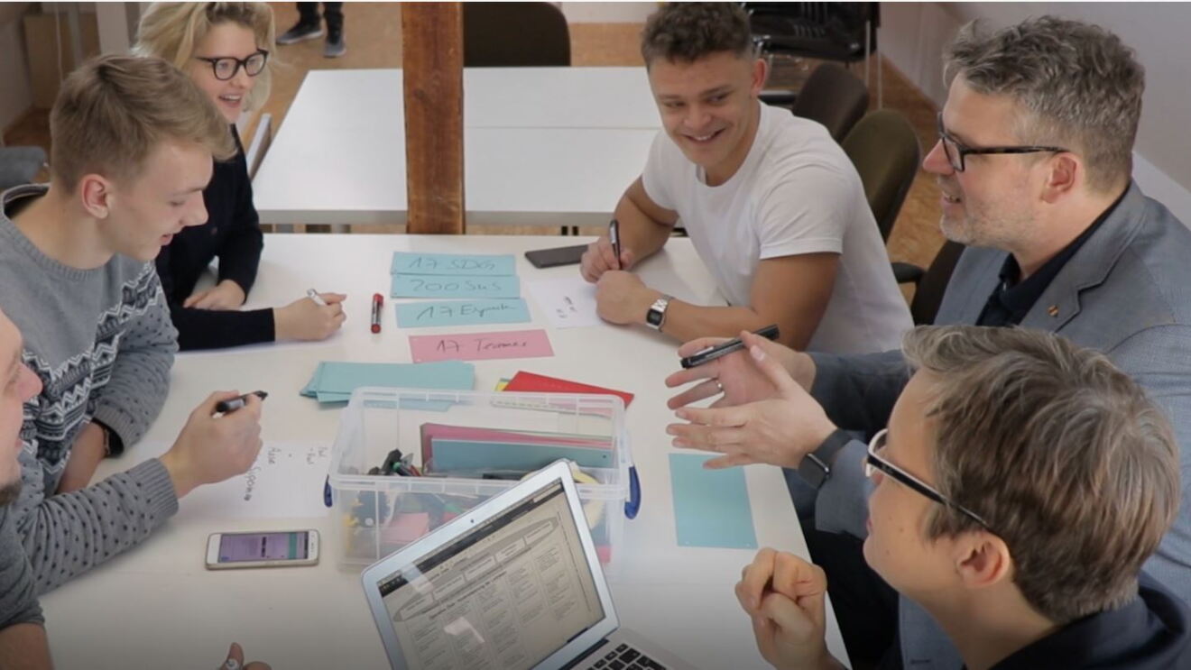 Das Team des politischen Podcasts etc.bp sitzen zusammen einen Tisch und erarbeiten Themen. Vor ihnen liegen bundete Post-its und Stifte. 