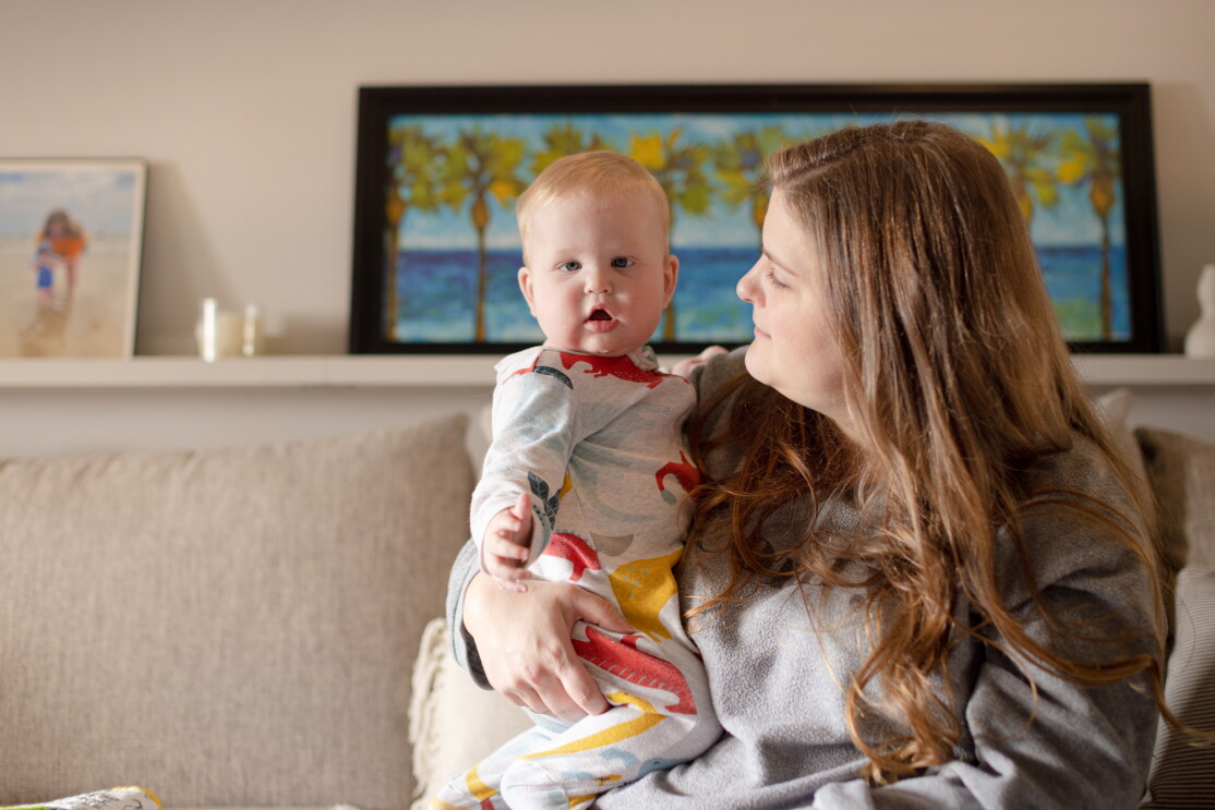 A woman sits on a couch and holds a baby.