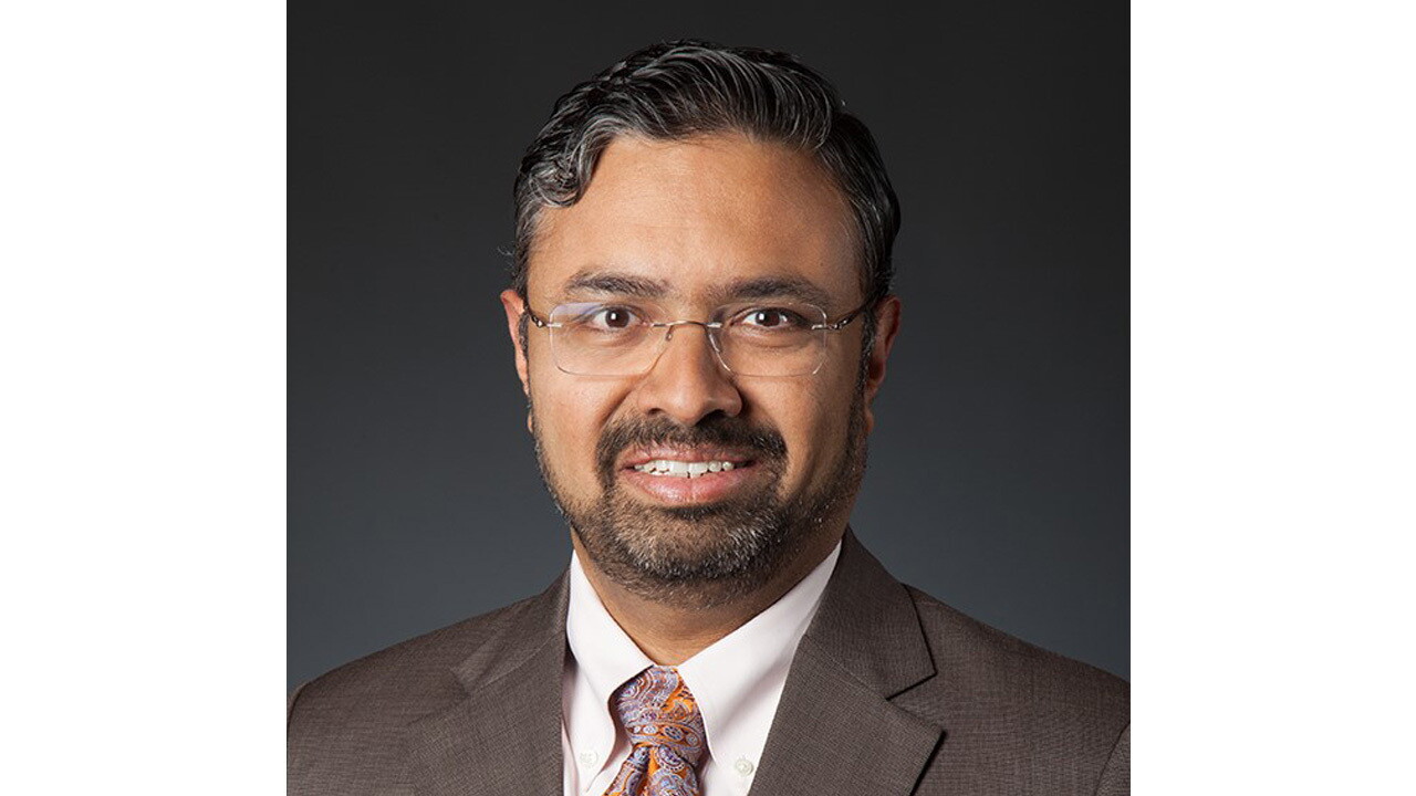 A headshot image of a man against a black background.