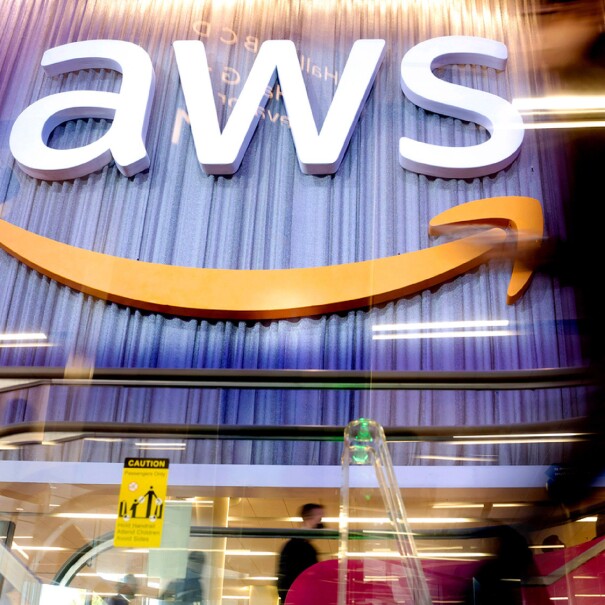 A photo of an AWS logo sign on the side of a conference center wall. There is an escalator handle in the forefront of the photo.