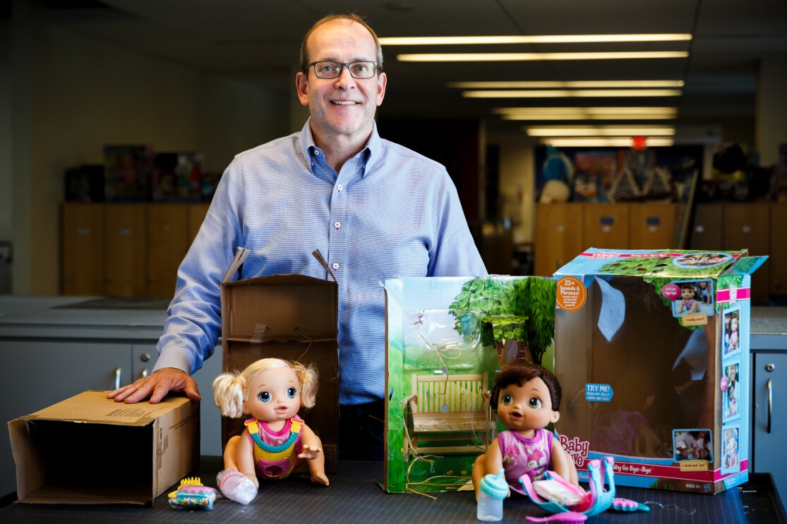 A man stands behind two toy boxes used to hold dolls.