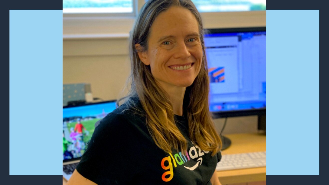 Amazon robotics employee Heidi smiles as she sits at her desk wearing a glamazon shirt.