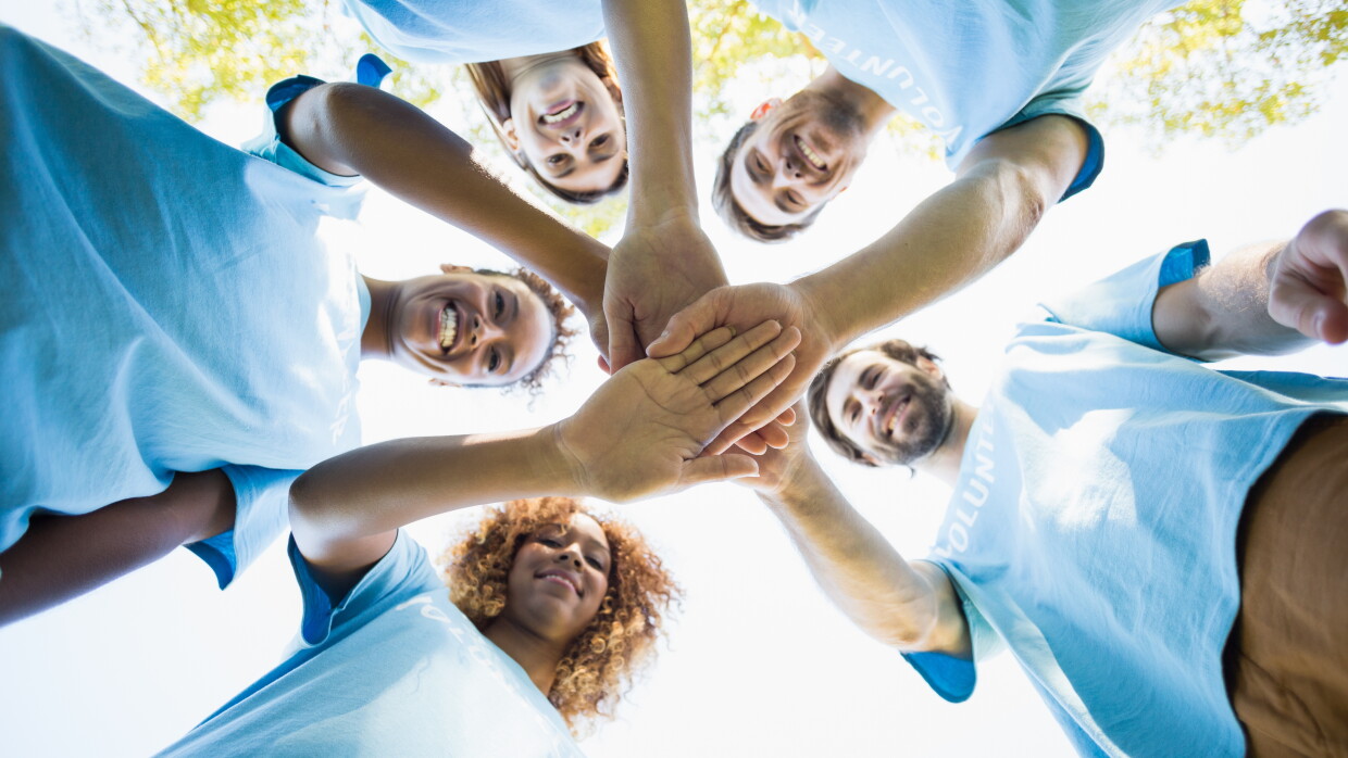 A group of people standing in a circle putting their hands together in the middle.