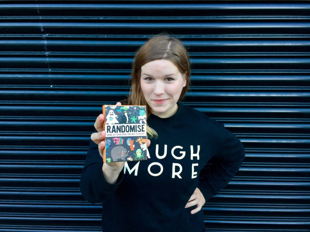 Gamely Games - Hazel holding up Randomise game to camera