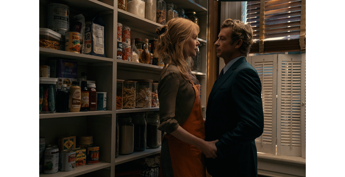 薄暗い収納スペースで食料品が並ぶ棚を背に、エプロンを着けた女性がスーツを着た男性と向かい合っている