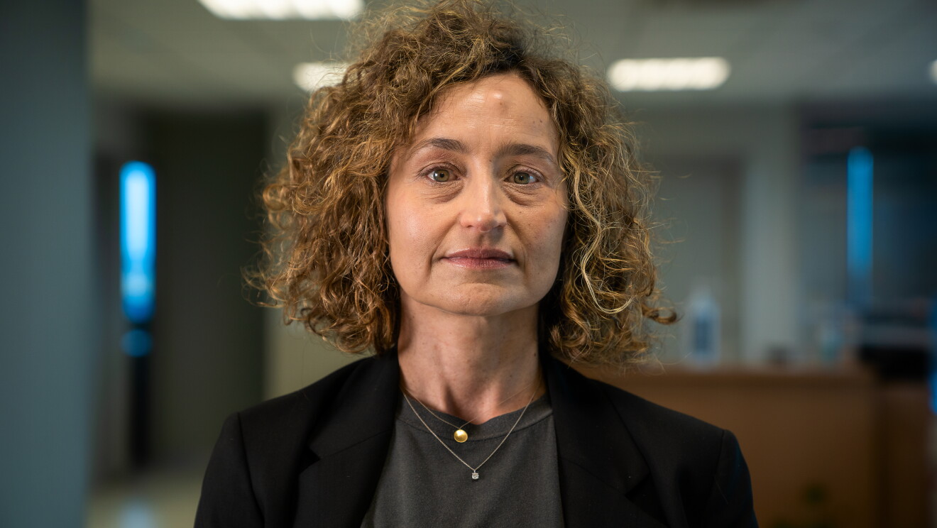 Mar Cid con dos collares, una americana negra y un jersey gris. Sonriente mira a cámara sin mascarilla. Tiene el pelo que casi le llega al hombro, rizado con mechas rubias. De fondo desenfocado lo que podría ser una oficina. 