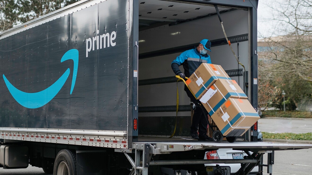 An Amazon DSP partner loads three boxes on a trolley into an Amazon delivery truck.