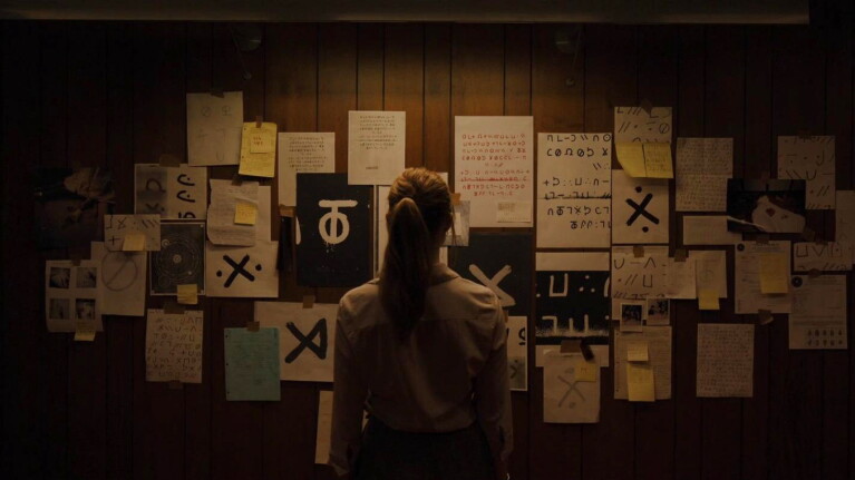 Investigator pondering wall covered in mysterious writings and symbols