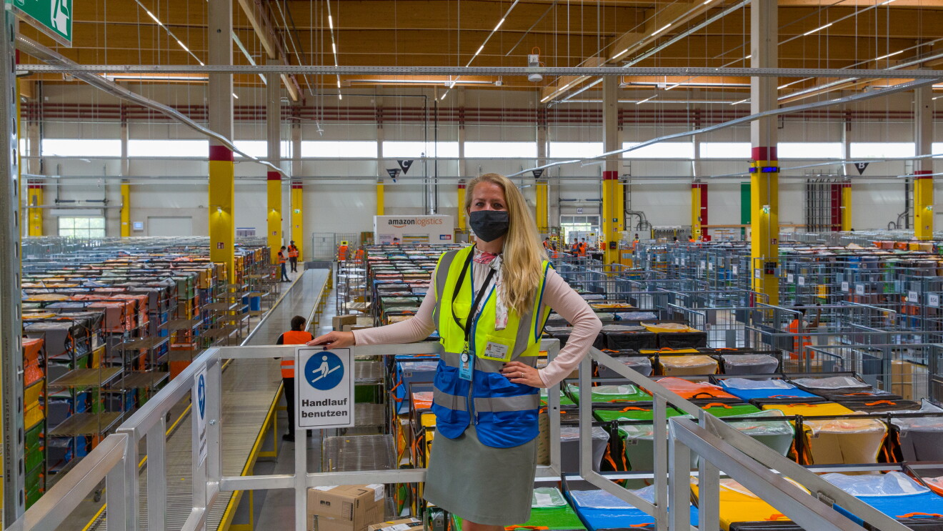 Eine blonde Frau mit Atemschutzmaske steht in einer Logistikhalle