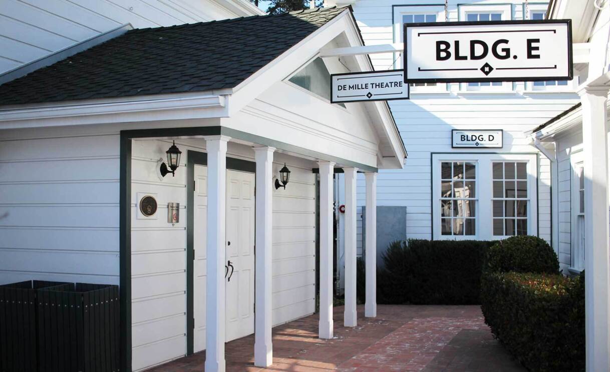An image of a white colonial-style building with a black roof. There is a sign that says "BLDG G"