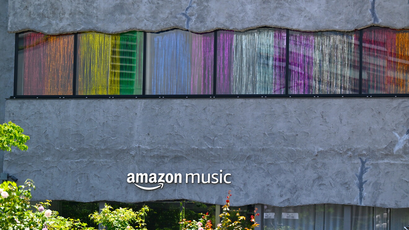 表面がざらざらとした灰色のビルにステンレス製のAmazon Musicのロゴ。その上の窓にレインボーカラーのカーテンがかけられている