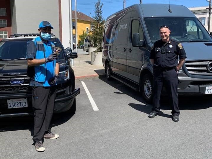 A police officer and a delivery driver stand near a delivery van.