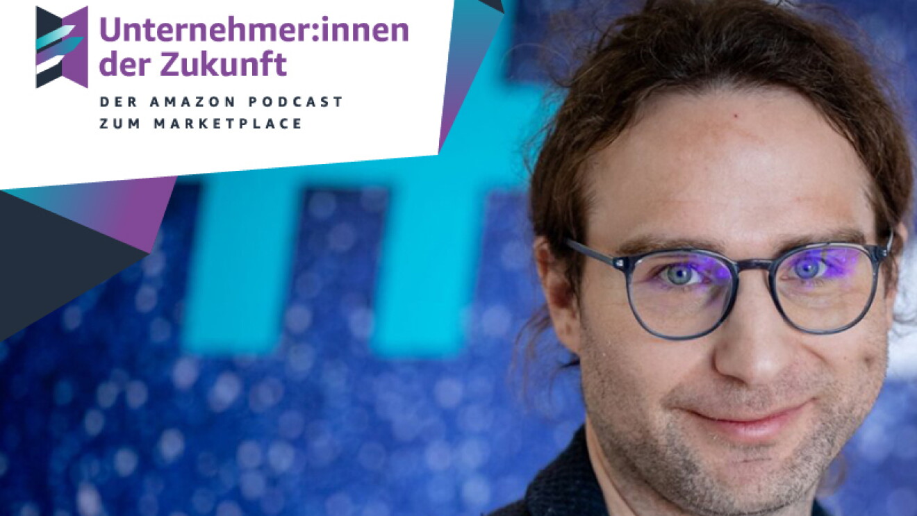Ein Mann mit braunen langen Haaren und einer Brille lächelt in die Kamera.