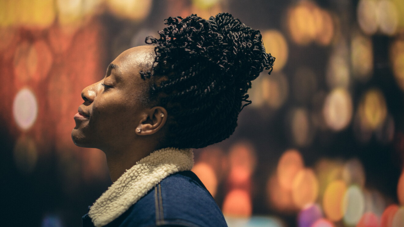 A woman in a blue jacket is photographed in profile. Her eyes are peacefully closed and she is looking skyward. 