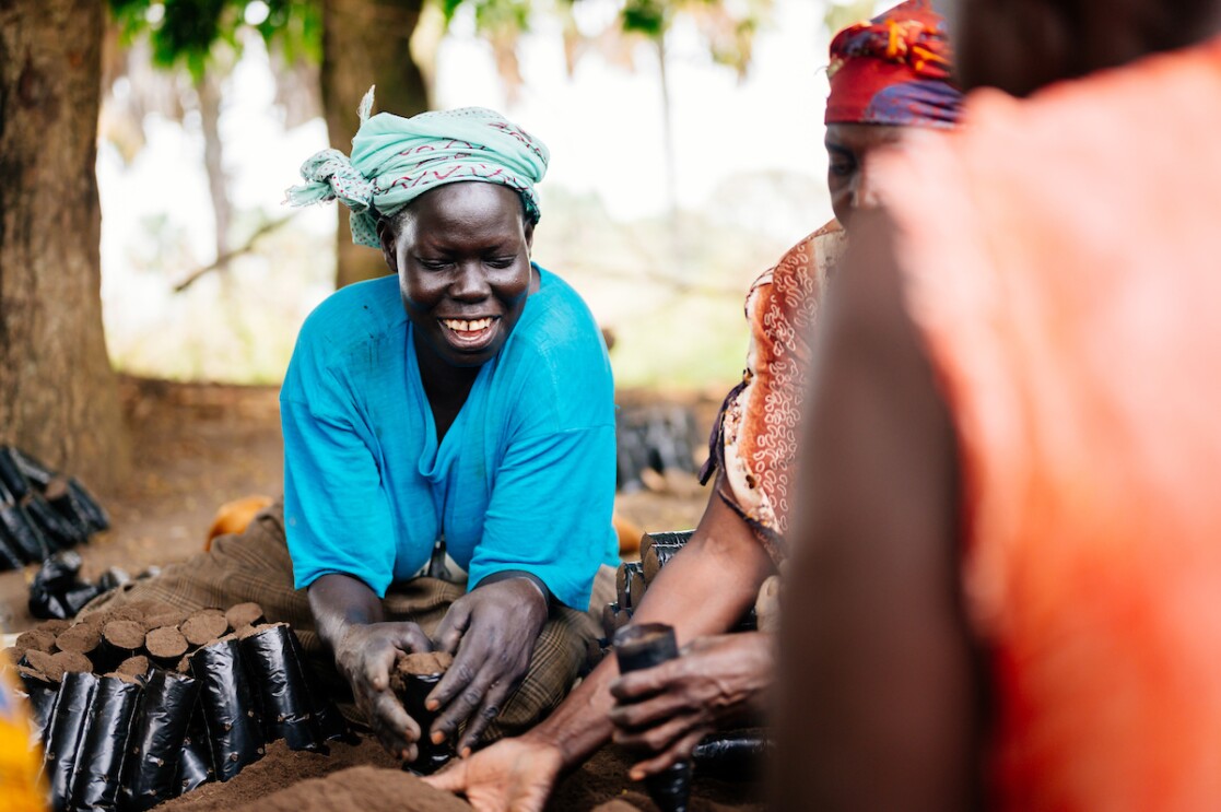 An image of a woman sitting in a group with other women planting trees and smiling.