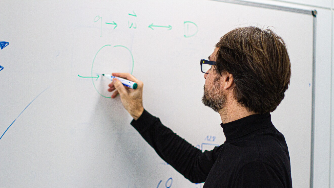 Hugo Zaragoza es investigador en el equipo Subjective NLP (Natural Language Processing) en Amazon Search. En una pizarra de pared Hugo está escribiendo con un rotulador verde. El lleva gafas, barba de una semana de color negra y blanca. Pelo por las orejas y jerseu negro de cuello alto. 