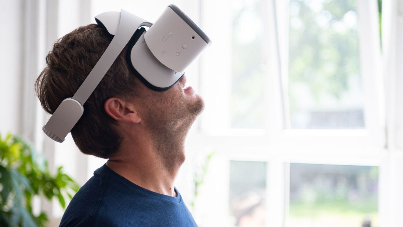Ein Mann sitzt vor einem hellen Fenster und schaut begeistert durch seine VR-Brille