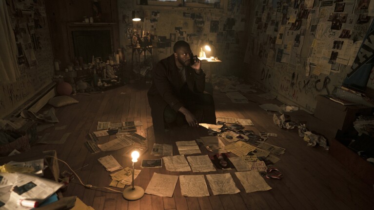 Prime Video’s Cross: Aldis Hodge as Alex Cross examining scattered evidence in dimly lit, cluttered room