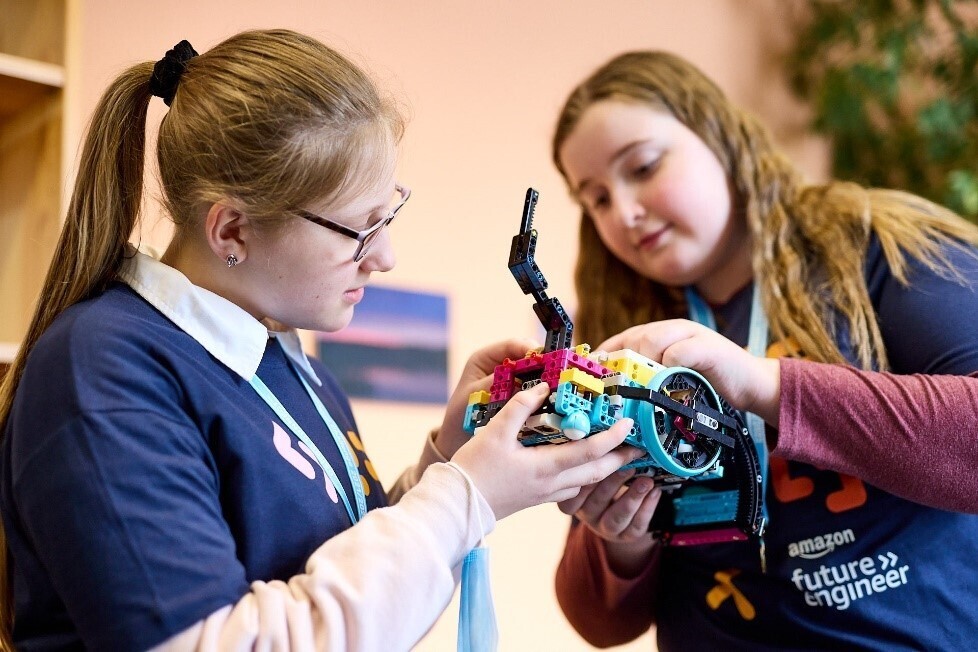 Zwei Schüler:innen arbeiten beim FIRST LEGO League Wettbewerb an ihrem Roboter und Forschungsprojekt. Auf der T-Shirt einer Schülerin ist Amazon future engineer geschrieben.