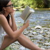Mujer leyendo al lado de un río.