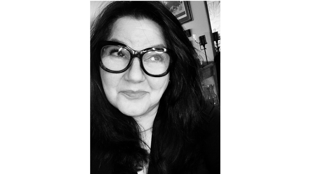 Bettina smiling and looking up in a selfie. She wears black framed glasses in a black and white photo.