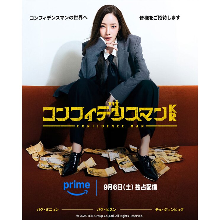 ジャケットにネクタイ、黒いパンツ着用の女性が、赤褐色のソファの背もたれ部分に腰かけ、座面に散った紙幣を靴で踏んでいる。中央に黄色い文字で「コンフィデンスマンKR」。