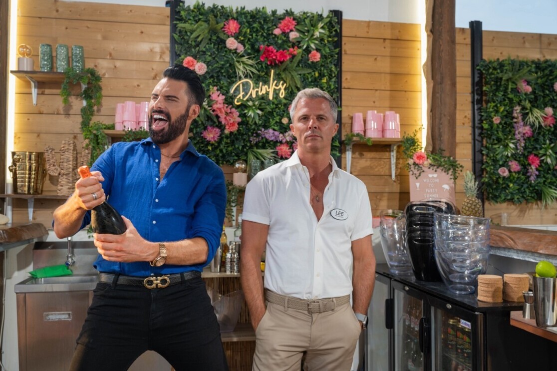 Two middle aged men stand in a bar