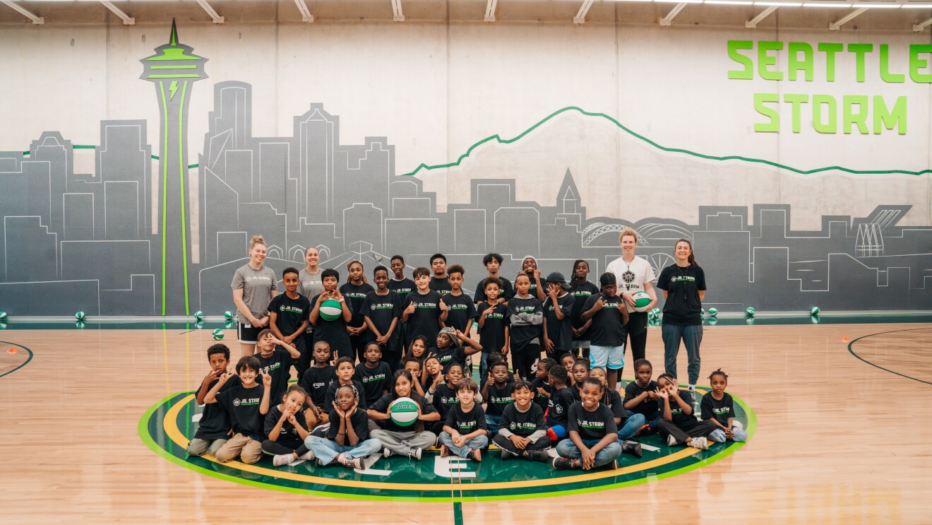 Children in black shirts pose on Seattle Storm logo with city skyline backdrop