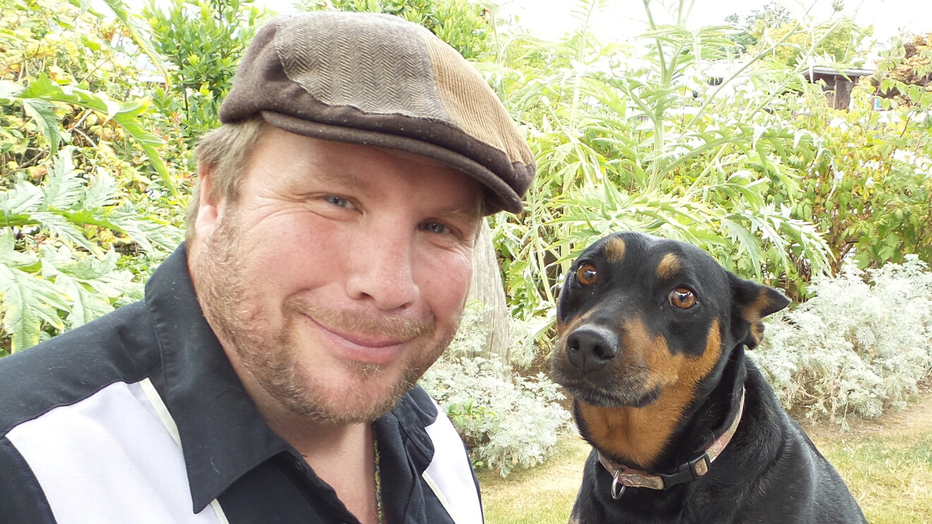 An Amazon author in a cap in the woods with his brown and black dog.