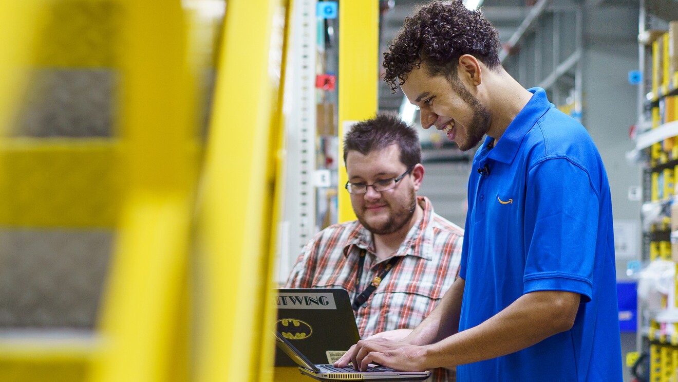 Two men stand side by side working on laptop computers. 