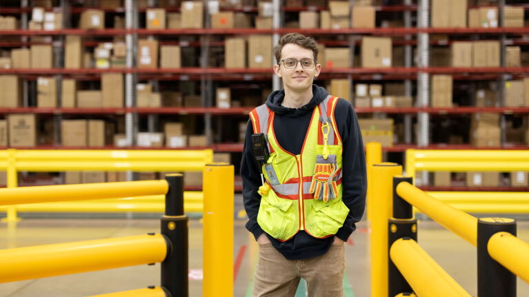 Young man in protective gear posing in front of warehouse shelving.
