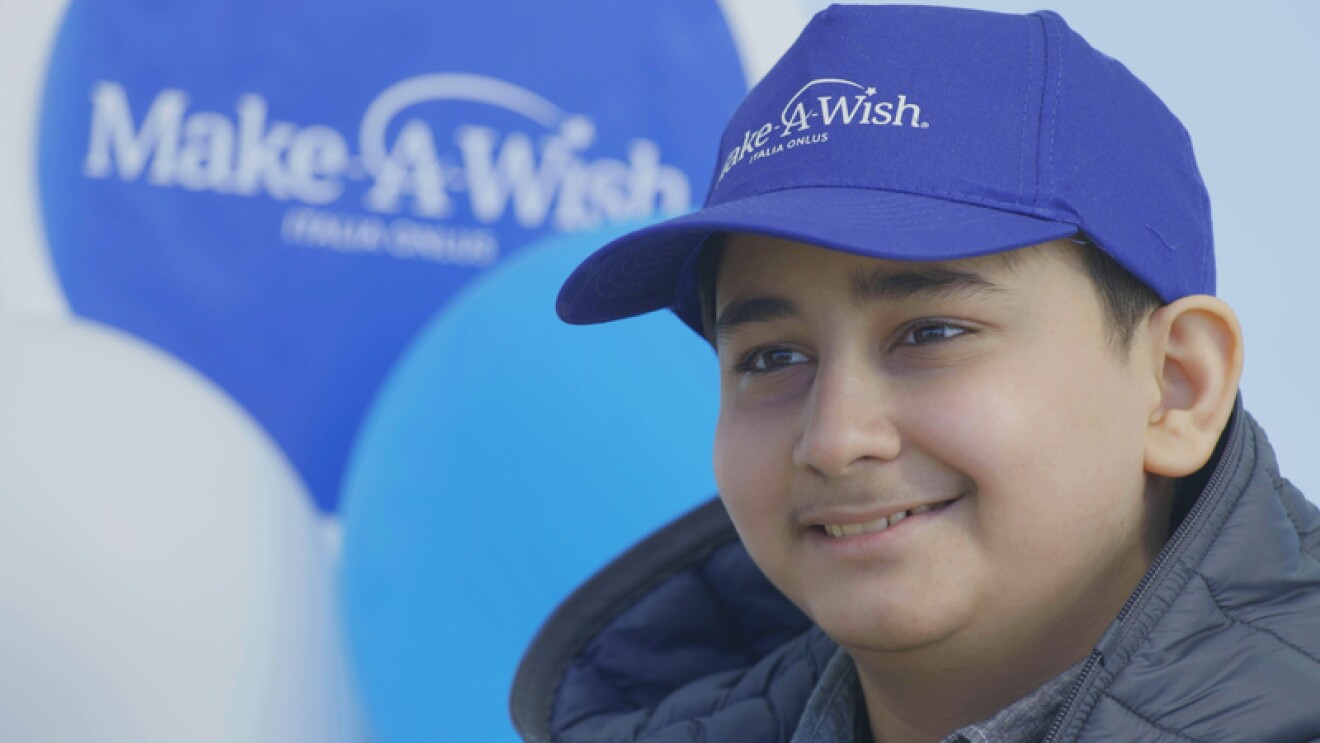 Hadi, uno dei bambini che hanno visto un desiderio realizzato grazie a Make-A-Wish, sorridente con un cappellino blu Make-a-Wish