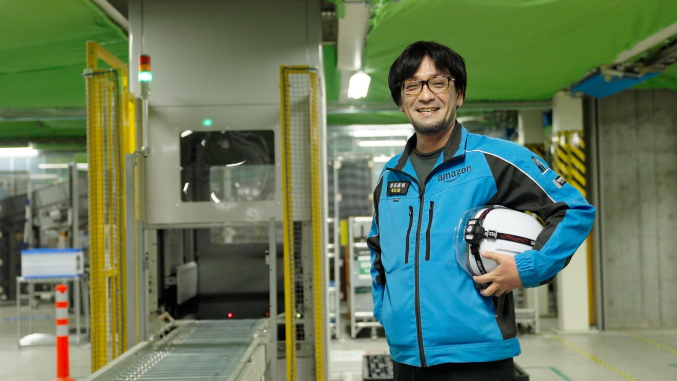 青い作業服を着てヘルメットを持って立つ男性