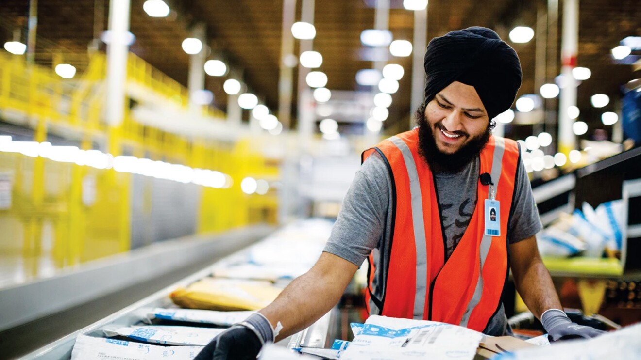 A man wears an orange safety vest and works in an Amazon fulfillment center.