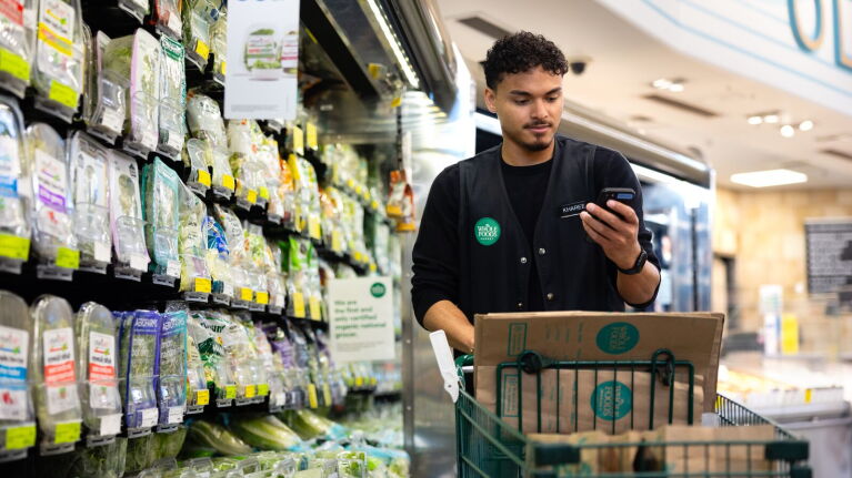 Whole Foods Market employee checking phone while holding delivery box in produce section