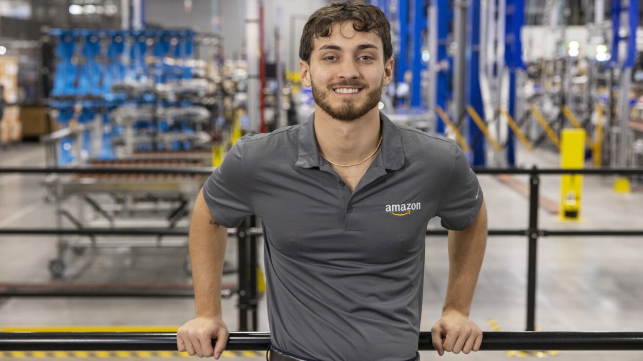 An Amazon employee smiles and stands in a fulfillment center.