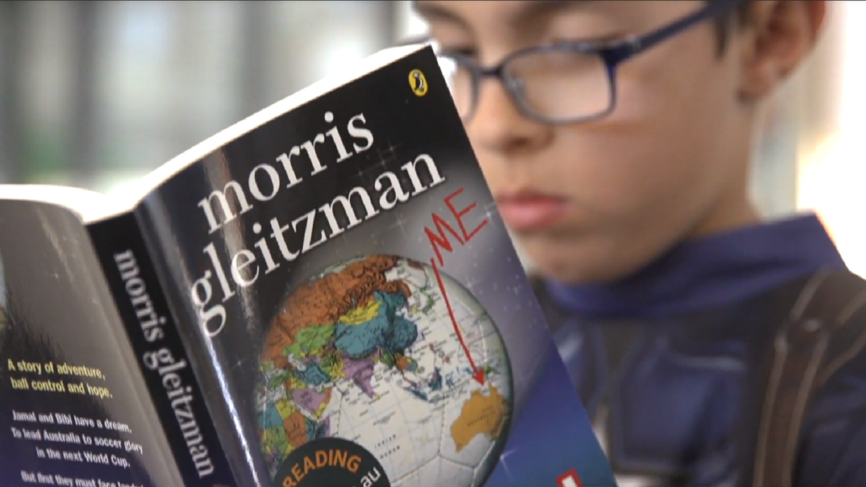 A child wearing glasses reads a book by Morris Gleitzman.