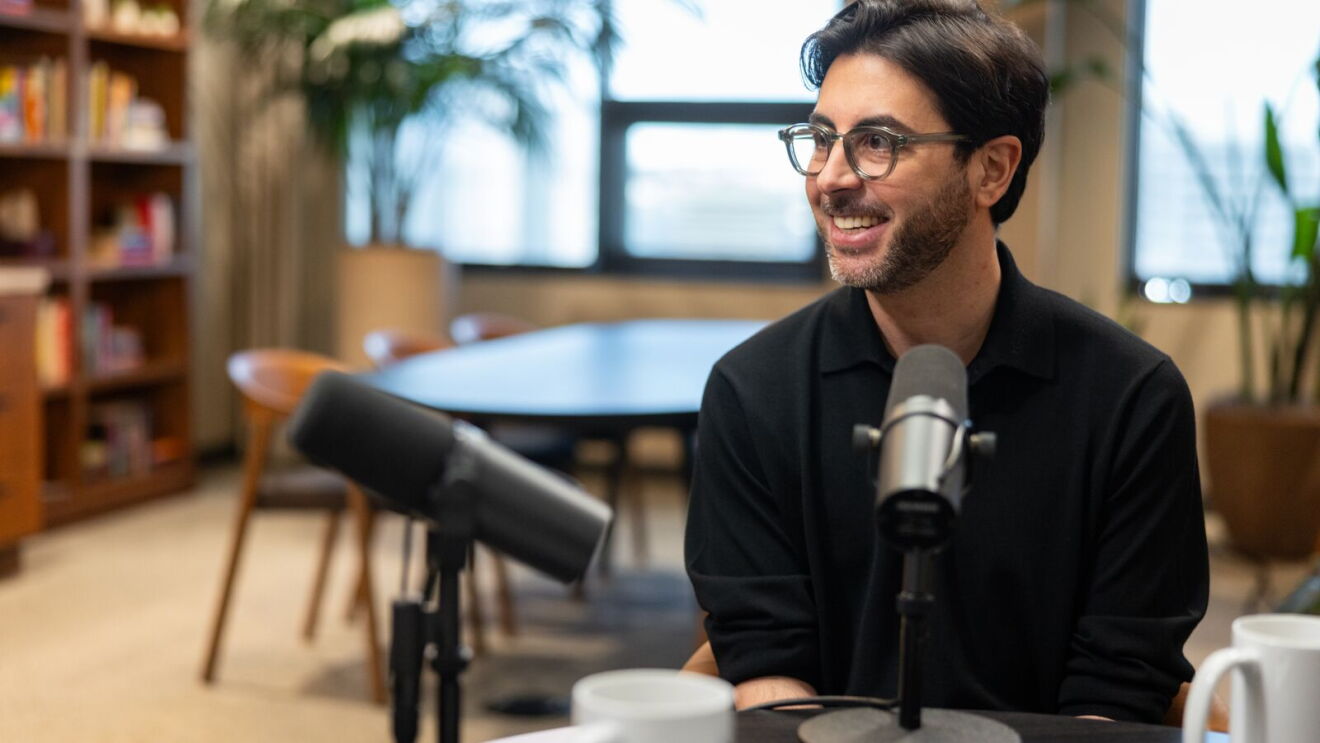 Amazon Fulfillment Center GM, Alessandro Carbone, in conversation during a podcast recording on Doug Herrington's podcast, with microphones positioned in front of him in a modern office setting.