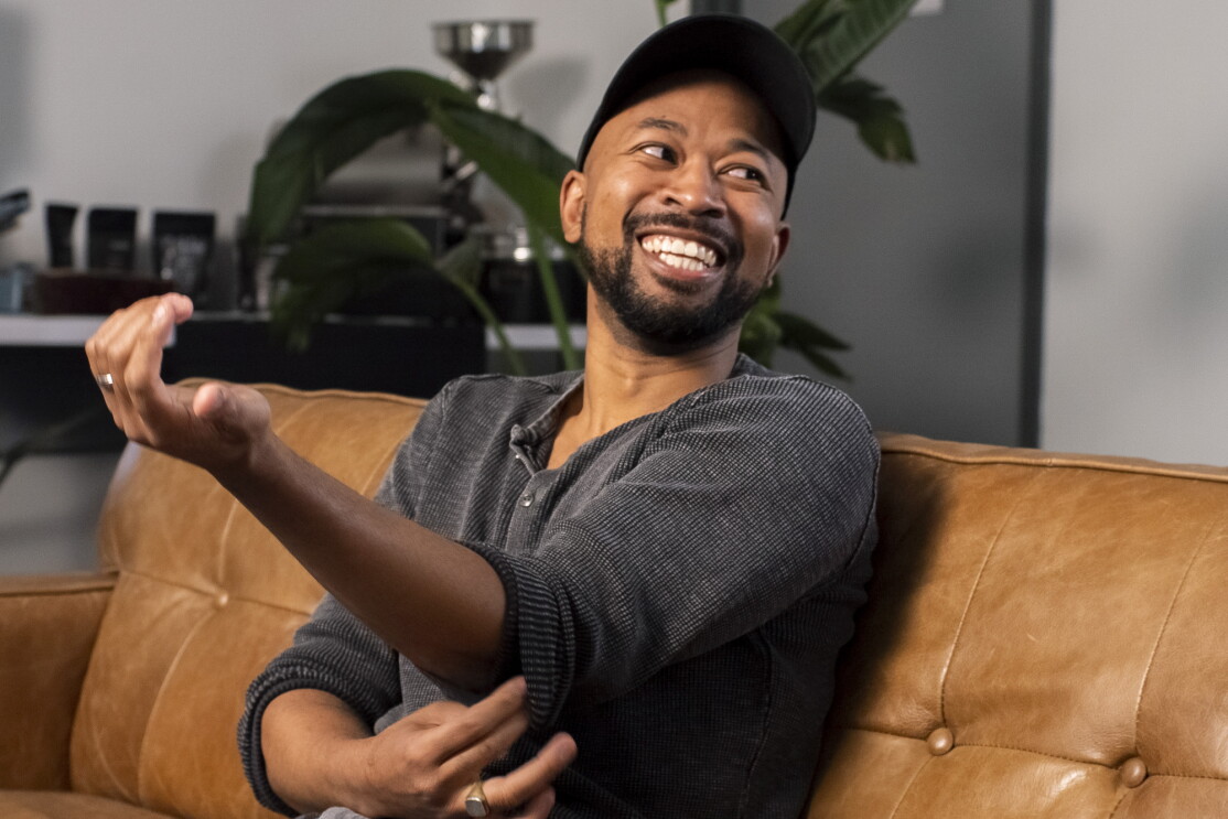 A smiling man in a baseball cap sits on a couch.