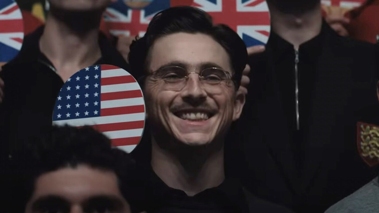 A man smiles as he holds a ping-pong paddle with a U.S. flag