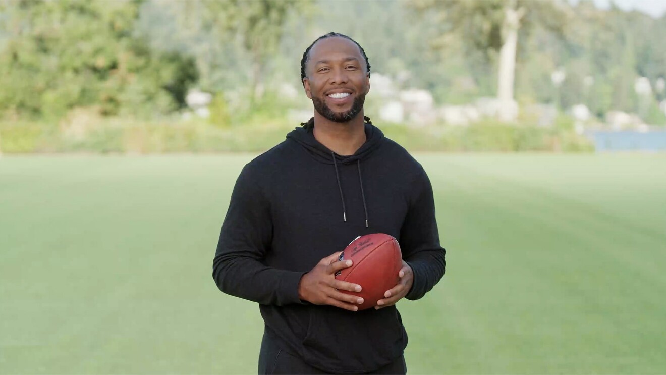 A photo of Larry Fitzgerald standing on a football field, holding a football.