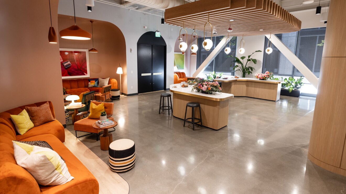 The cafe area inside the Amazon Music studio in Los Angeles. There is a large counter space with stools in front of the coffee bar. There are also several seating nooks, and two big black doors at the end of the space that lead into the rest of the studio.