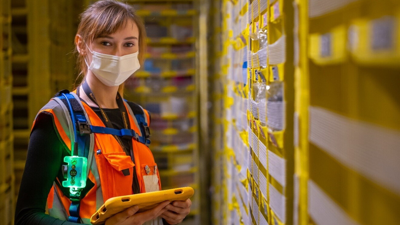 Arbeitsplatz in Gera. Mitarbeiterin, die eine orangene Weste und eine Maske trägt, mit Tablet in der Hand.