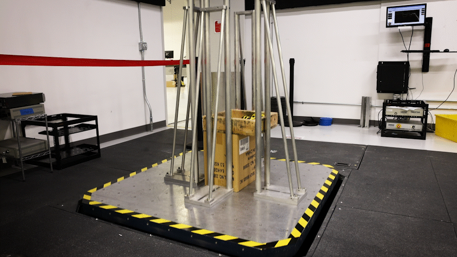 An animated gif of a large metal plate moving up and down slightly off the ground with several boxes in the middle of it.