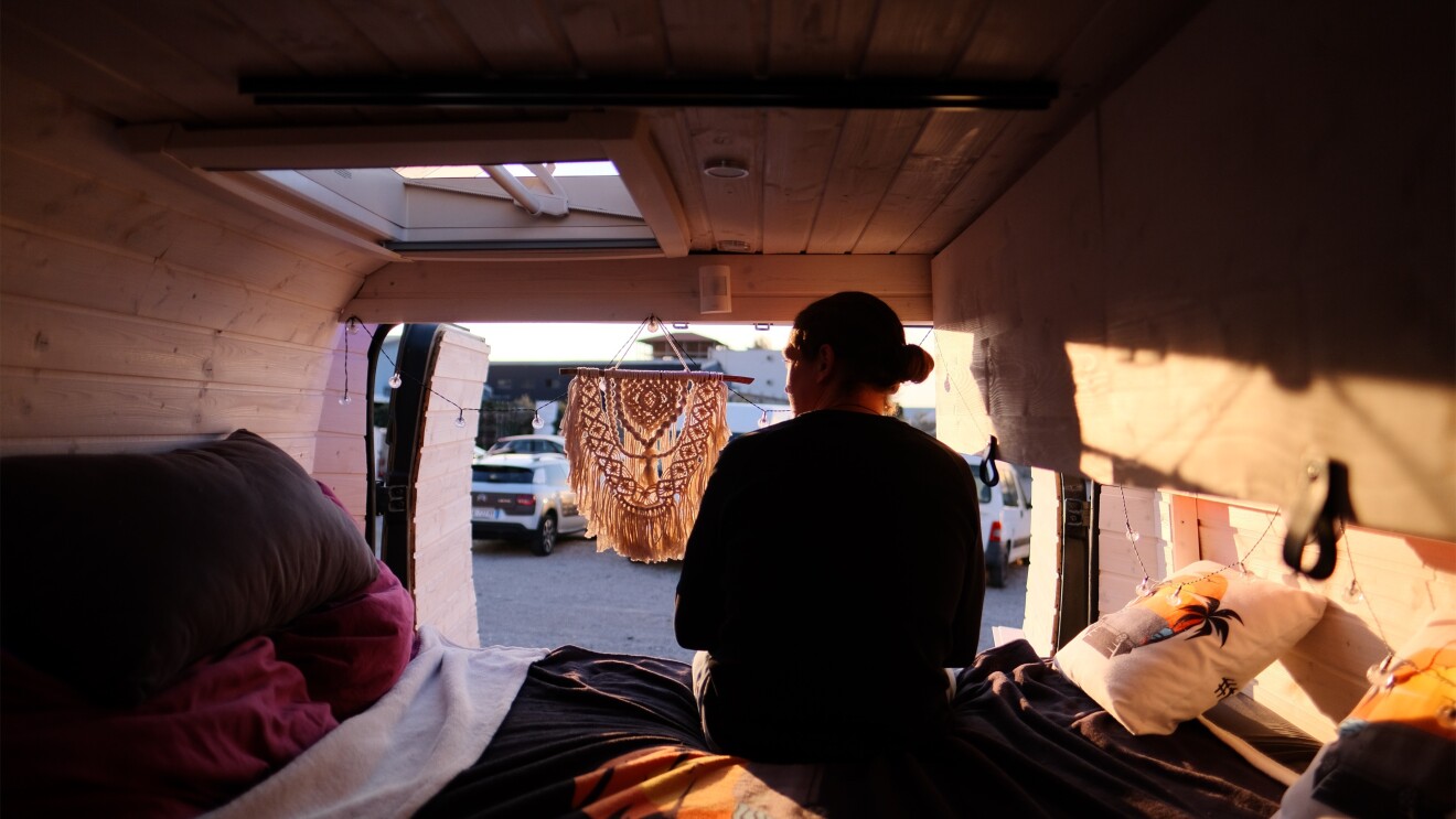 Ein Mann mit Zopf sitzt in seinem Camper Van. Er sitzt mit dem Rücken zur Kamera und wir von der Sonne angeleuchtet.