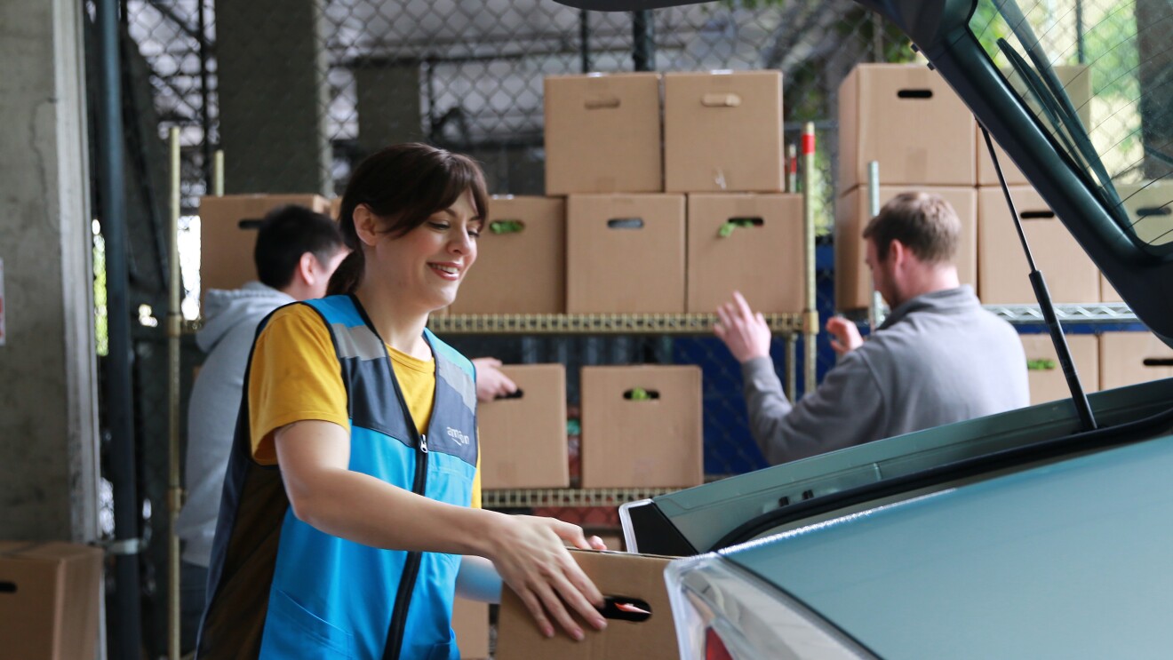 Volunteer in blue vest smiling while loading boxes into car