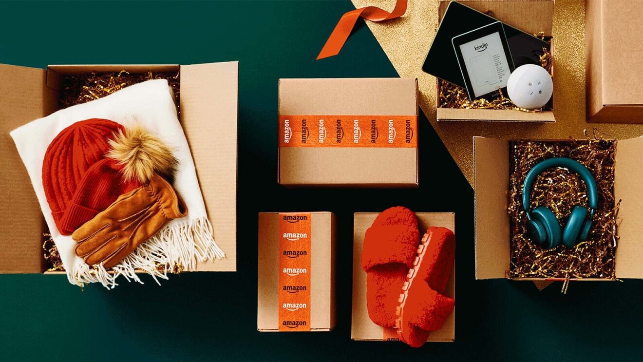 An assortment of opened and unopened Amazon boxes display a variety of great holiday gift ideas, from a Kindle to a pair of fuzzy red slides.