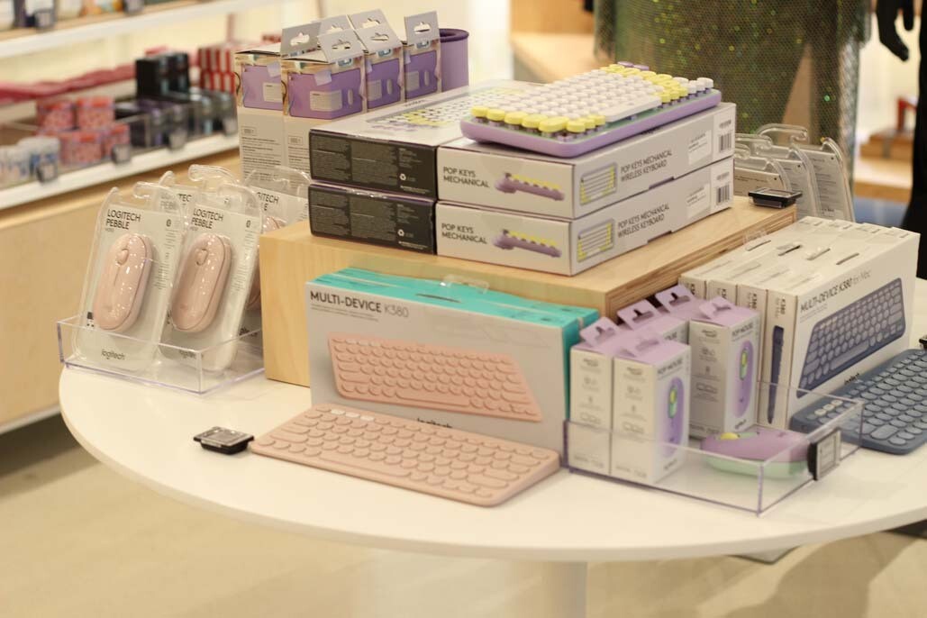 An image of a shelf of items to work from home, including a keyboard, a computer mouse, and various other boxed items in pinks, purples, and pastel colors.