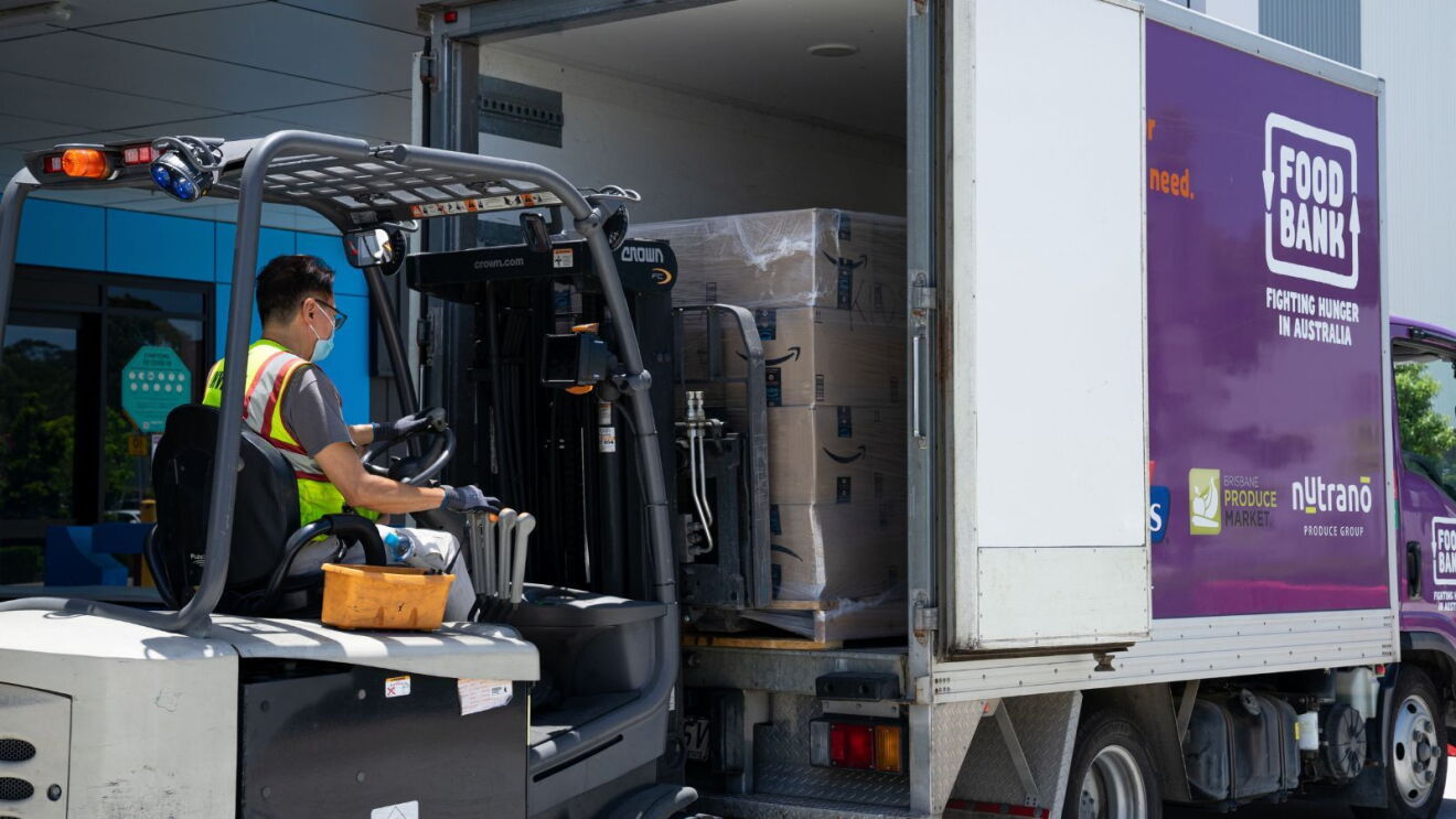Man driving a loader to load relief supplies into a Food Bank truck as part of Amazon's disaster relief efforts in Australia.