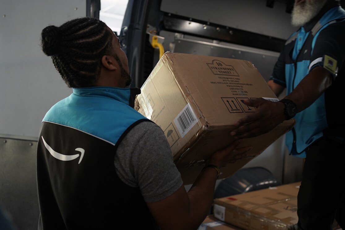 Volunteers and Amazon employees load up Amazon delivery vans with essential furniture and household products.